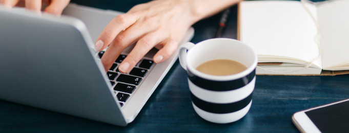 A woman typing with coffee at a desk